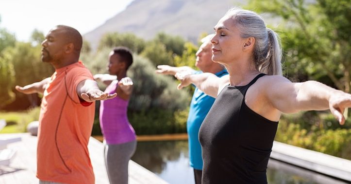 A group of individuals each doing the same yoga pose in front of a mountain-filled landscape