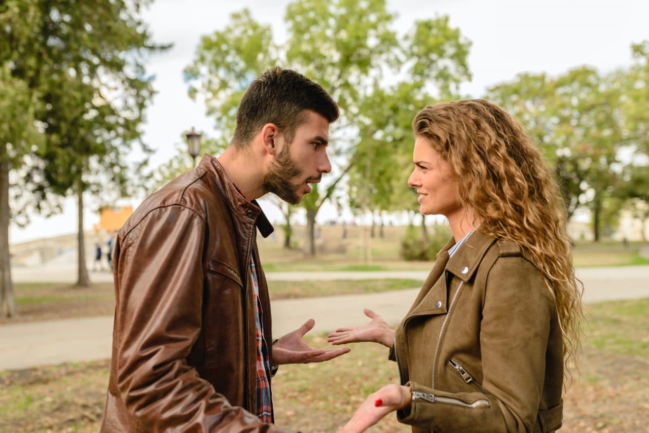 man and woman facing each other arguing in a park