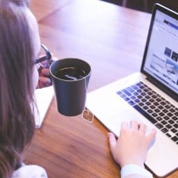 Woman holding a cup of tea while working on a laptop