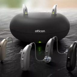 Oticon hearing aids in front of a charging base